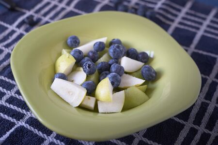Fresh fruit salad in a green dish on a blue cloth, close upの写真素材