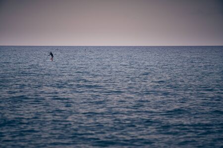 Stand up paddle boarder in wetsuit paddling on a sea. Minimalist imageの写真素材