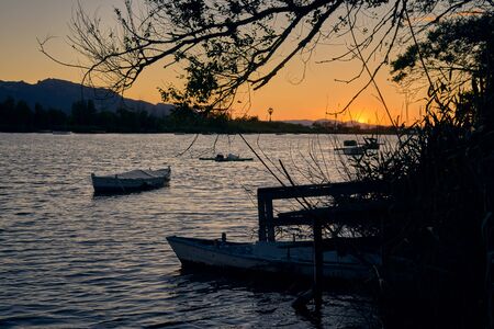 Impressive sunset on the lake from the jetty with some boats floating and a tree in the foreground...