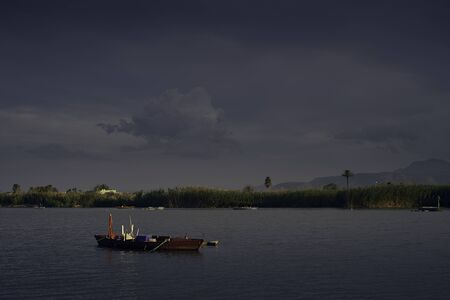 Sunset on one day cloudy in the famous lake of the albufera of Valencia, spain with a boat in the front.の写真素材