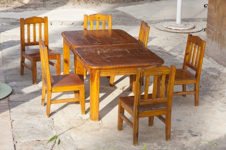 Outdoor cafe patio with old, shabby wooden tables and chairs in the sunlight photoの写真素材