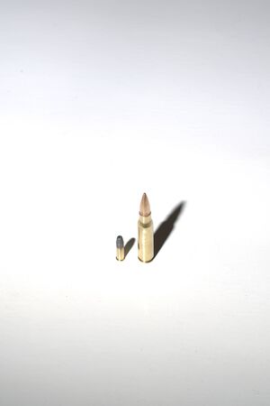 Two bullets of different calibers on white background with long, dark, dramatic...