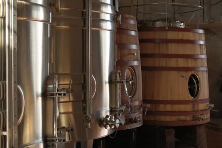 Wine tanks in a winery, some made of stainless steel, two others in the back made of wood.