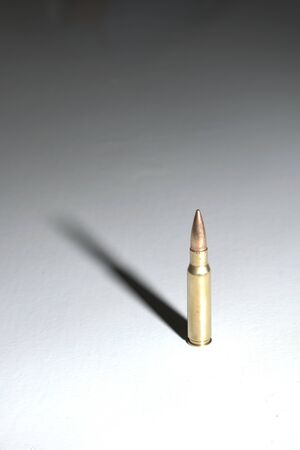 Assault rifle bullet (7.62 x 51 mm NATO) on a white surface with long dramatic shadow. Dark...