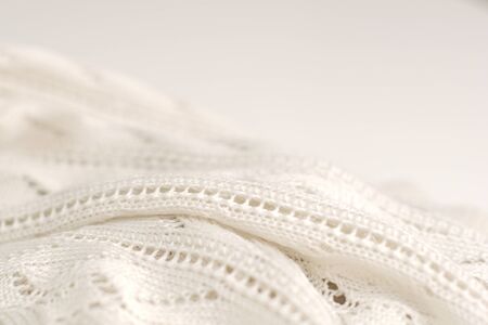 Ivory color crochet sweater on white background. Texture detail close up. High key lighting
