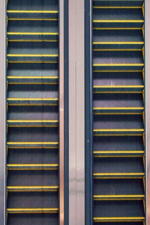 Parallel steel escalators at an airport, top-down elevated view.