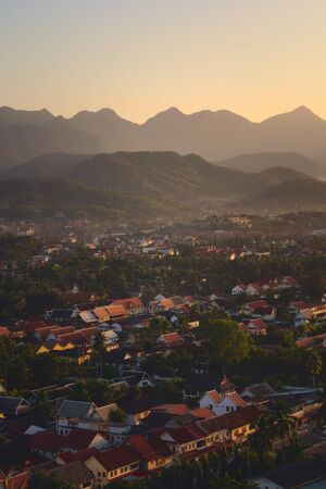 Elevated view of the city of Luang Prabang, Laos, at sunset, with mountains on the background.