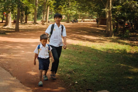2019-11-15 / Siem Reap, Cambodia - Two boys in school uniform walk down a dirt road in a rural area.のeditorial素材