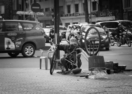 2019-11-12 / Ho Chi Minh CIty, Vietnam - A man repairing an old bicyle on a sidewalk. Black and white.のeditorial素材