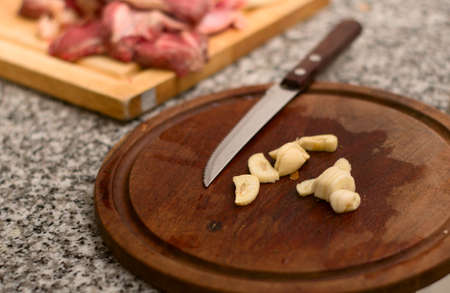 Sliced garlic on a wooden plate with red meat in the background. Close up.の写真素材