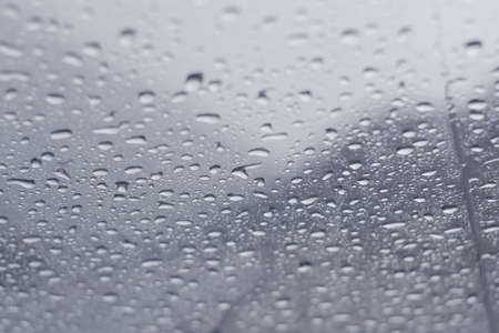 Raindrops dripping across a window in a cold winter day. Close up, texture background.