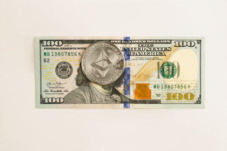 Physical Ethereum coin over a one hundred dollar bill. Cryptocurrency exchange, investment concept.の写真素材