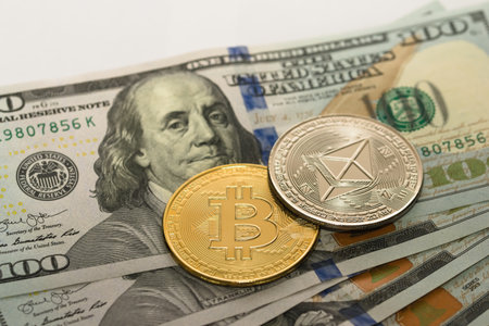 Physical Bitcoin and Ethereum coins over some one hundred dollar bills. Cryptocurrency exchange, investment concept.の写真素材