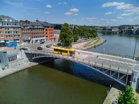 Yellow bus crossing a bridge over Sambre river in Namur, Belgium, on a sunny day. Aerial view.の写真素材