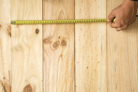 Hand holding tape measure to measure on wooden backgroundの写真素材