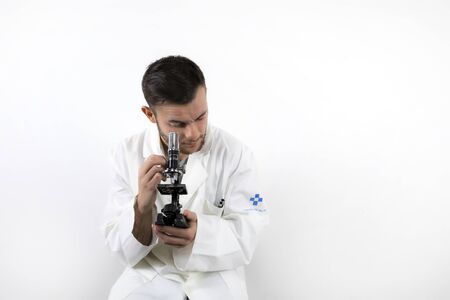 Young male doctor with beard looking through microscope isolated on white background
