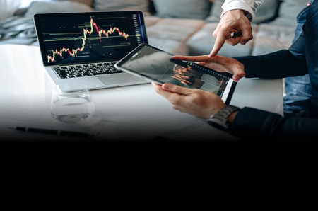 two people working on laptop and tablet computer with stock market graph on screen in modern officeの写真素材