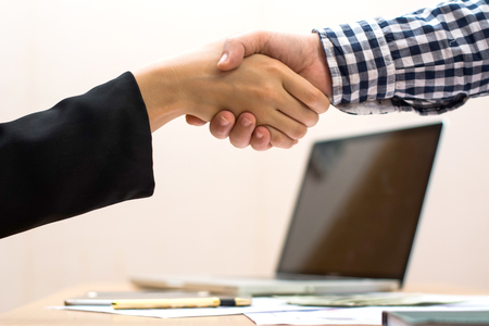 Two business women shaking hands while carrying smart devices in their other hands. Selective focus image with blurred city view as background.の写真素材