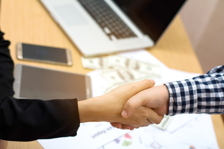 Two business women shaking hands while carrying smart devices in their other hands. Selective focus image with blurred city view as background.の写真素材