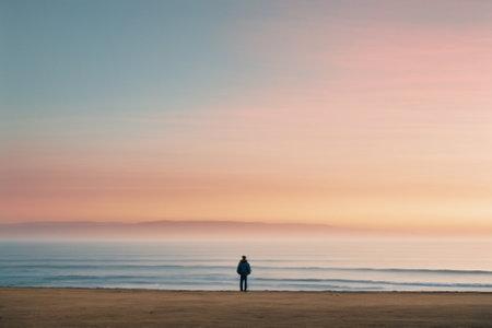 A man stands on the beach and looks at the sea at sunsetの素材
