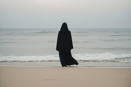 Muslim woman in black niqab walking on the beach with sea background.の素材