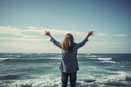 Back view of young woman with arms outstretched standing on the beachの素材