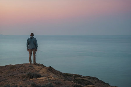 Man standing on the edge of a cliff and looking at the seaの素材