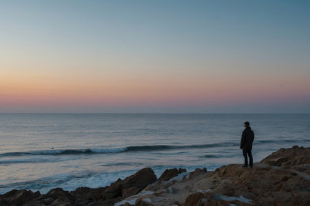 Man standing on the rock and looking at the sea at sunset.の素材