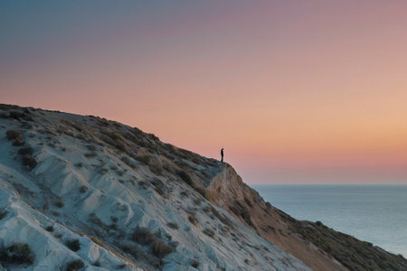 Silhouette of a man standing on the edge of a cliff at sunsetの素材