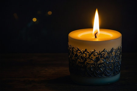 Burning candle on wooden table in dark room. Copy space.の素材