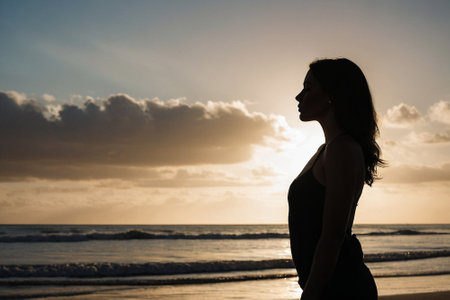 Side view of young woman looking away while standing on beach at sunsetの素材