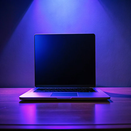 Laptop with blank screen on table in dark room illuminated by blue lightの素材