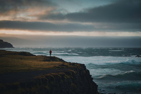 A man standing on a cliff and looking at the ocean in Icelandの素材