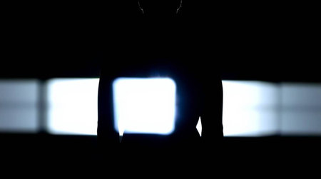 Silhouette of a man in a dark room illuminated by a light beamの写真素材