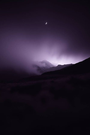 Mountain landscape at night with the moon and stars in the cloudsの写真素材