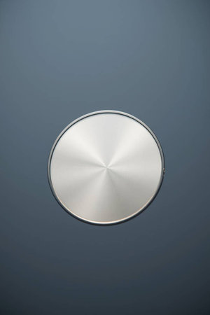 A round stainless steel button isolated against a gray background with copy space