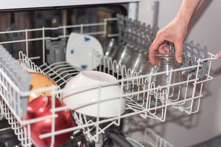 Close up view of a womans hand loading the dishwasher. Shallow DOF, selective focus on the hand.のeditorial素材