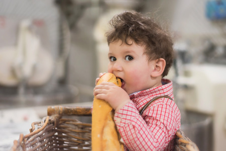 Portrait of a cute baby inside a basket with bread in the bakeryの写真素材