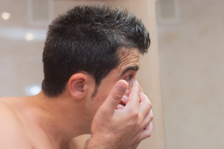 Young man putting contact lens in his eyeの写真素材