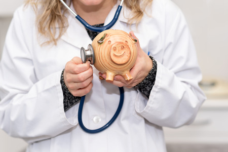 Financial check up. Doctor holding piggy bank checking with stethoscopeの写真素材