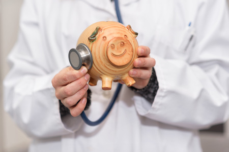 Doctor holding piggy bank close up. Medical insurance and health care money concept.の写真素材