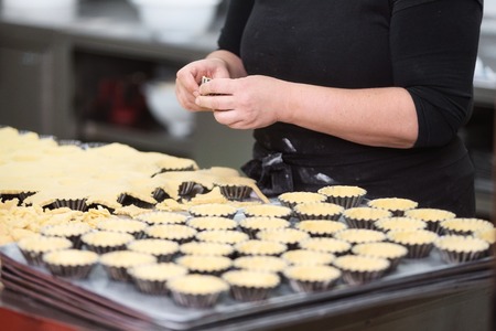 Pastry chef making tartlets, putting the dough in baking dishes, at kitchen of pastry shop.