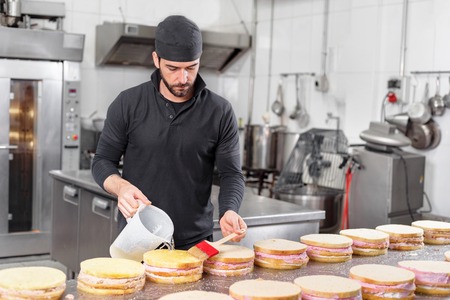 Handsome professional confectioner making a batch of delicious cake in the pastry shop.