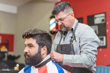 Handsome bearded man getting haircut by hairdresser at the barber shop.の写真素材