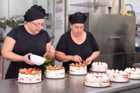 Two woman pastry chefs working together making cakes at the pastry shop.の写真素材