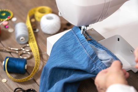 Close-up of senior woman hands seamstress sewing jeans on electrical sewing machine.の写真素材