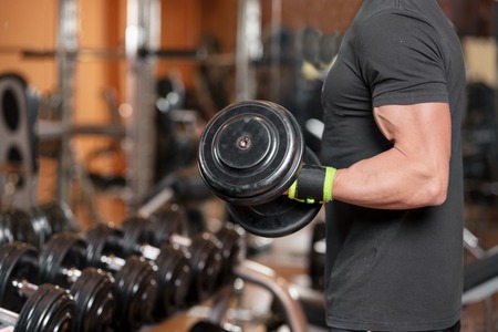 Muscular man working out in gym doing exercises with dumbbells at biceps, strong male.