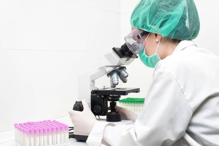 Young female scientist in modern laboratory, using microscope.