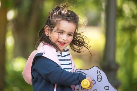 Cute girl enjoying on playground in the park in summertime.