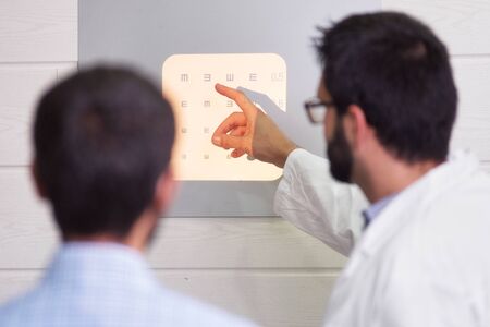 Ophthalmologist pointing at letters while patient is reading the eye chart.